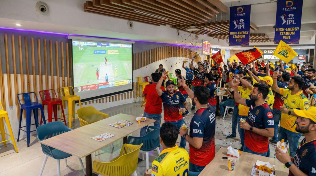 A large crowd cheering with flags during the Live screening of Tata IPL in Noida at D Square Food Court.